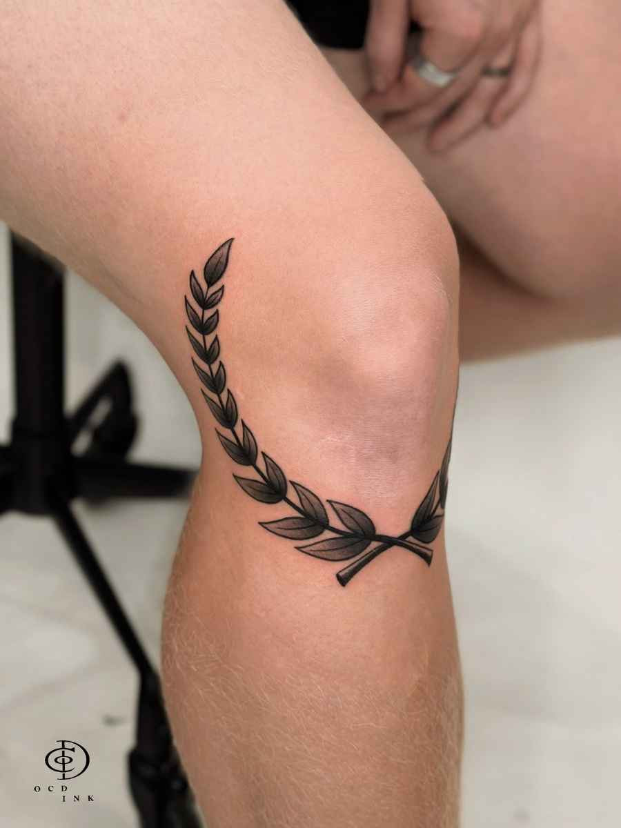 Blackwork Blackwork tattoo of a laurel branch wrapping around the knee with bold leaves and smooth shading