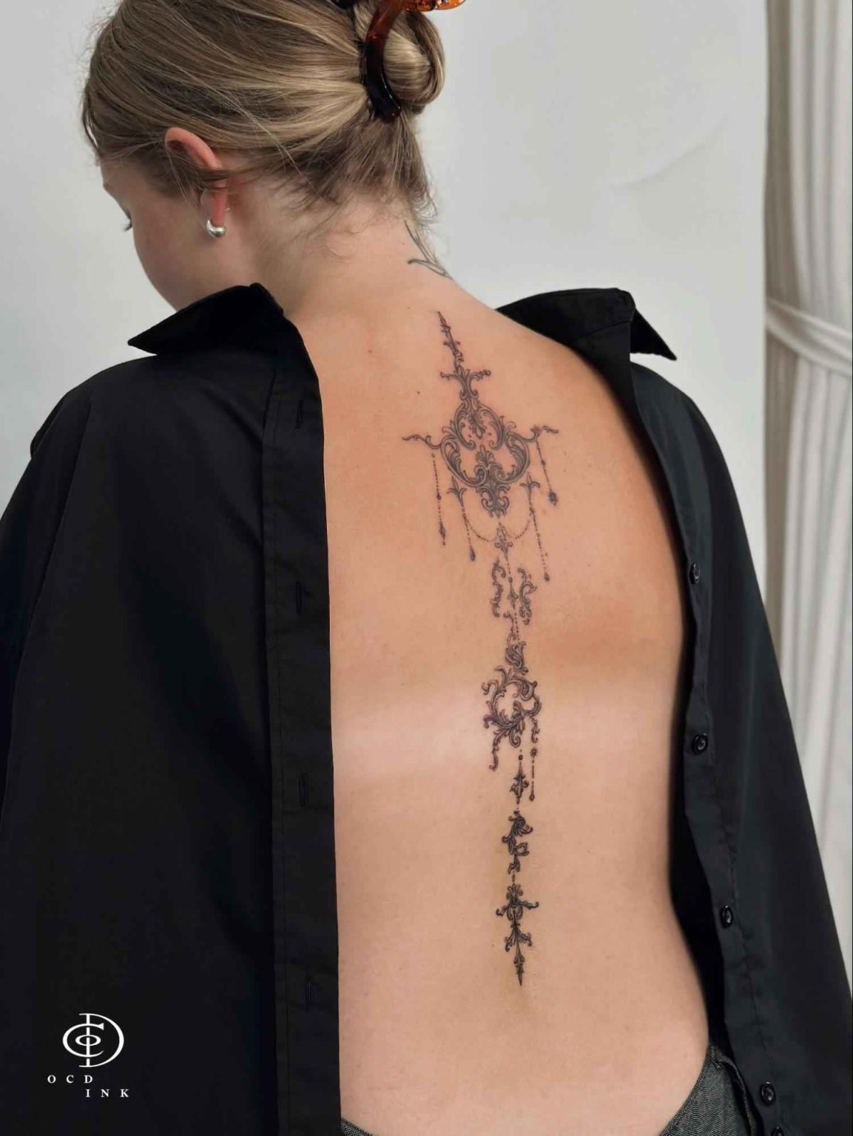 Ornamental chandelier spine tattoo featuring intricate filigree details, decorative chains, and elegant vertical symmetry