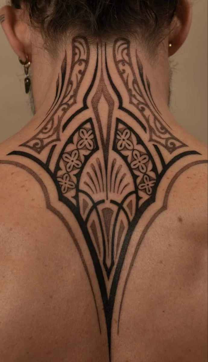 Ornamental tattoo with tribal patterns featuring symmetrical blackwork, floral motifs, and flowing neck-to-back linework