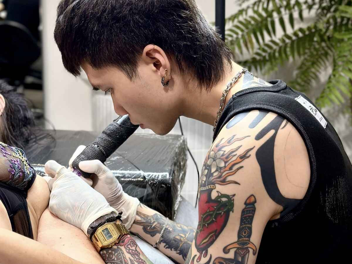A tattoo artist wearing gloves carefully works on a client's tattoo in a professional studio