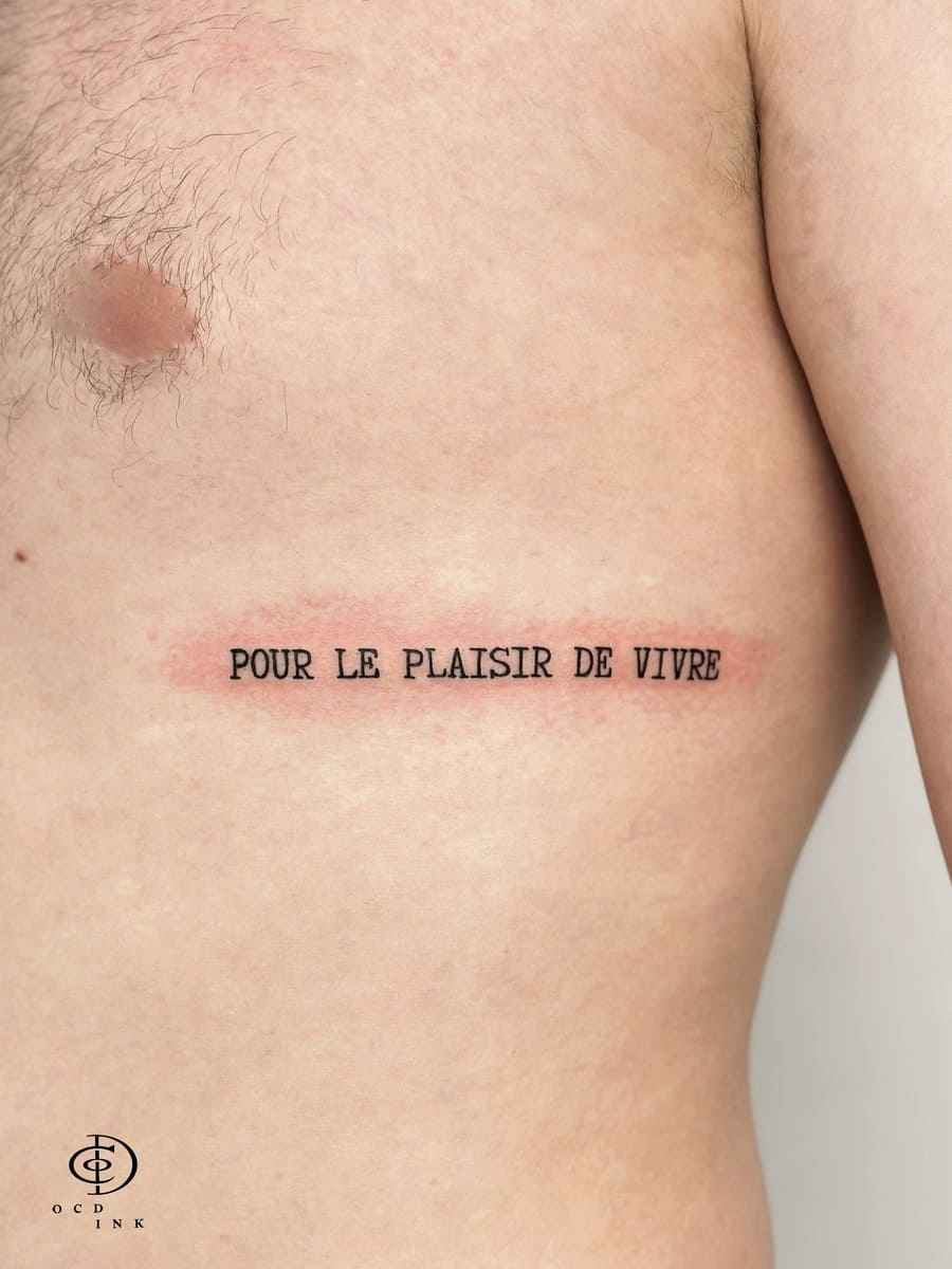 Typewriter font tattoo with French quote in black serif lettering along the ribcage