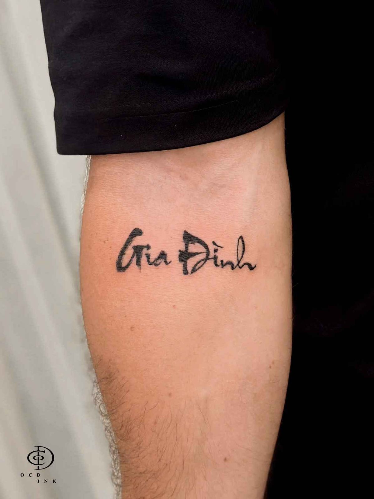 Vietnamese calligraphy tattoo reading "Gia Đình" in bold brush-style lettering on the upper arm