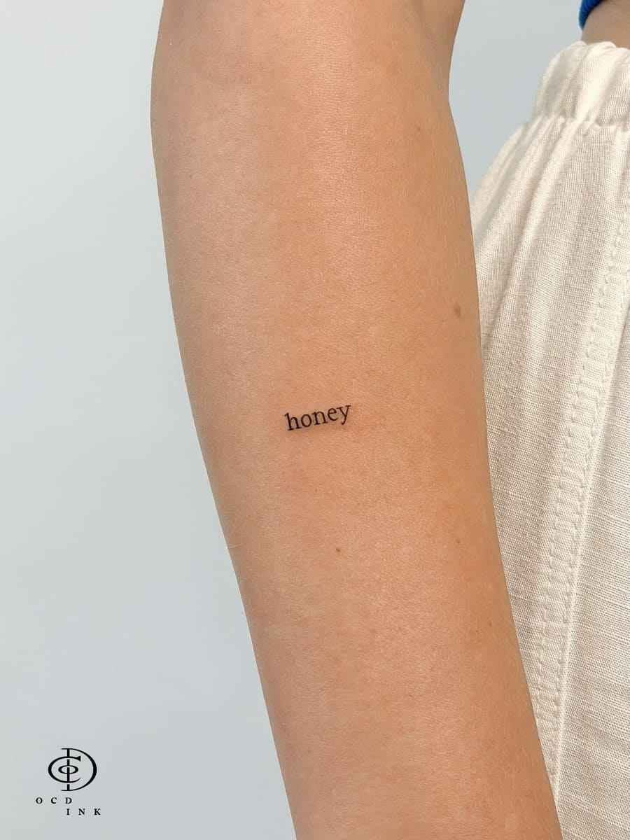 Tiny typewriter-style tattoo reading "honey" on the inner forearm