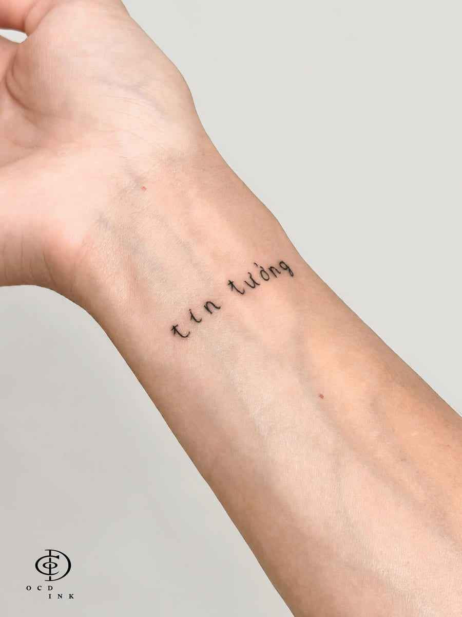 Fine line Vietnamese phrase tattoo reading "tin tưởng" on the inner wrist