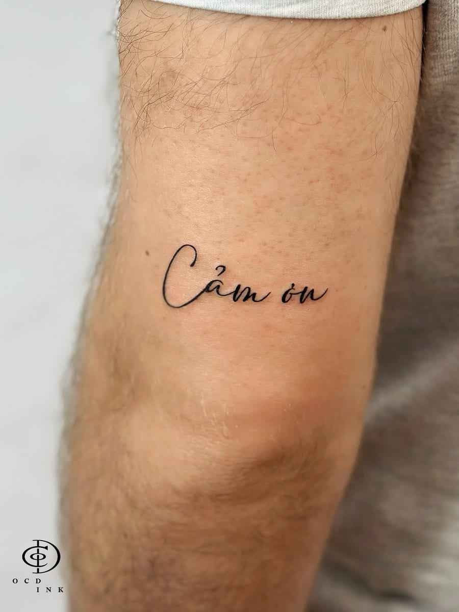 Vietnamese script tattoo reading "Cảm ơn" in elegant cursive lettering on the arm