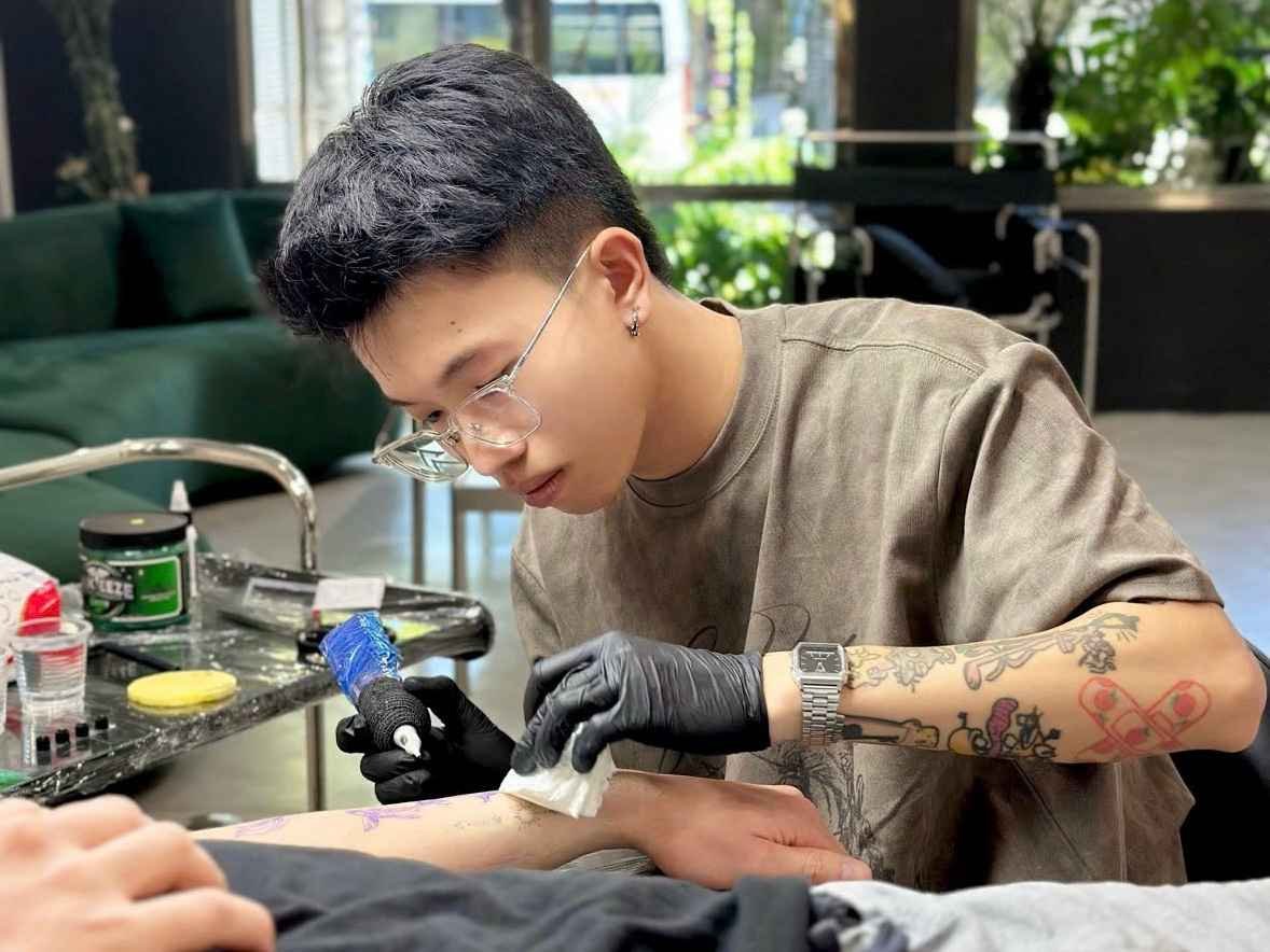 Professional tattoo artist preparing a client's forearm tattoo in a modern studio while wearing gloves and using a tattoo machine under sterile conditions.