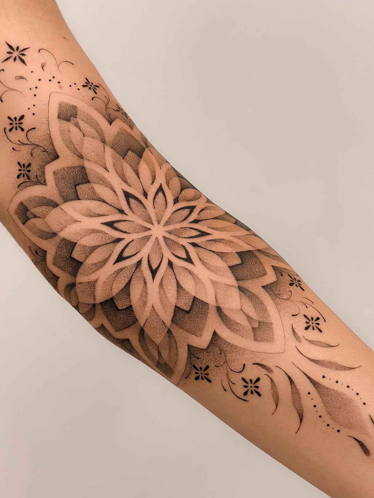 Mandala dotwork tattoo on the forearm featuring layered floral geometry, smooth stipple shading, and ornamental botanical accents in black and grey