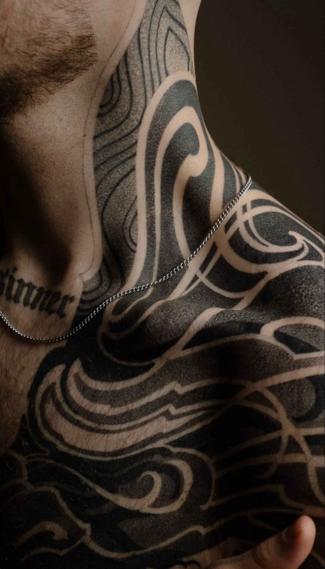 Negative space tattoo covering the neck, shoulder, and chest, featuring flowing abstract blackwork patterns with smooth dotwork shading and bold skin-break contrasts.