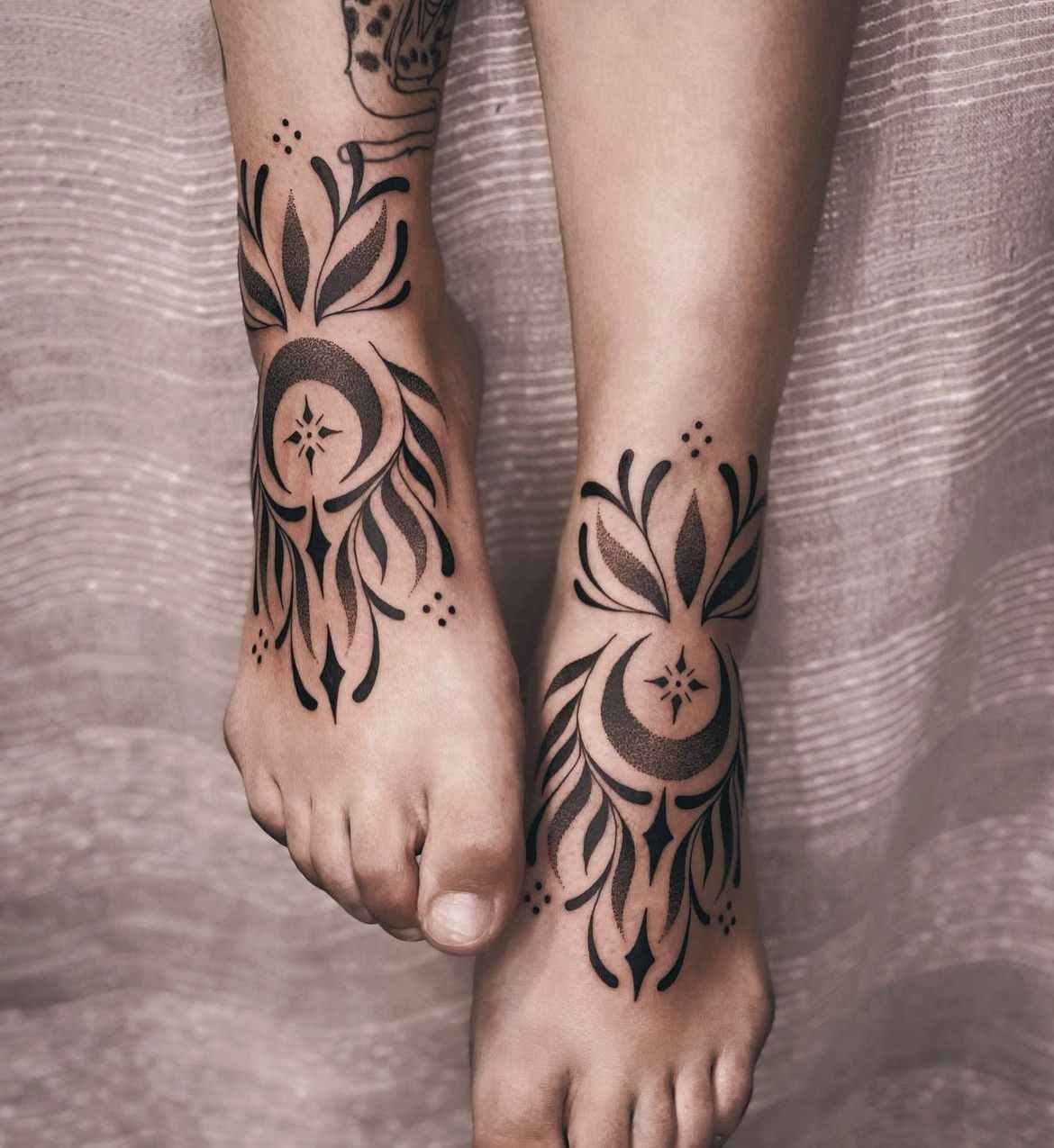 Matching ornamental dotwork tattoos around both ankles featuring crescent moons, botanical motifs, bold blackwork accents, and soft stipple shading.