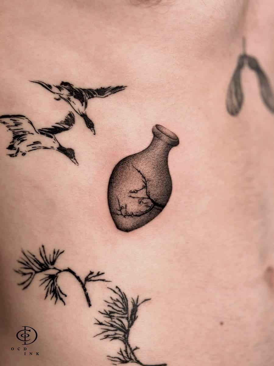 Dotwork tattoo of a minimalist ceramic vase containing delicate tree branches, rendered with fine stipple shading and subtle black and grey gradients on the torso.