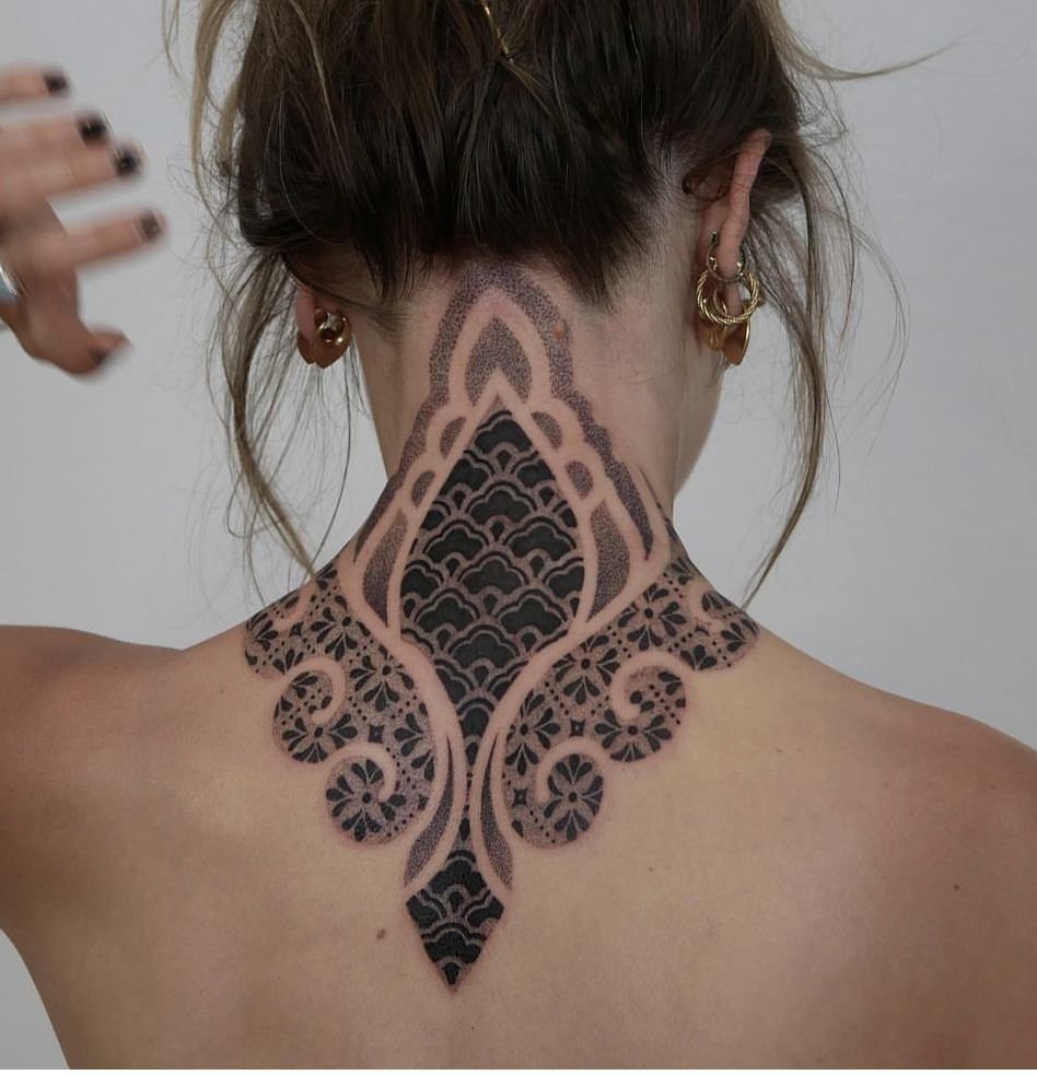 Ornamental dotwork tattoo extending from the back of the neck to the upper back, featuring symmetrical decorative motifs, bold blackwork panels, and fine stipple shading.