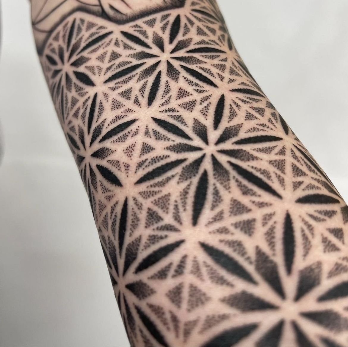 Detailed forearm tattoo featuring a repeating geometric dotwork pattern made of interconnected floral shapes
