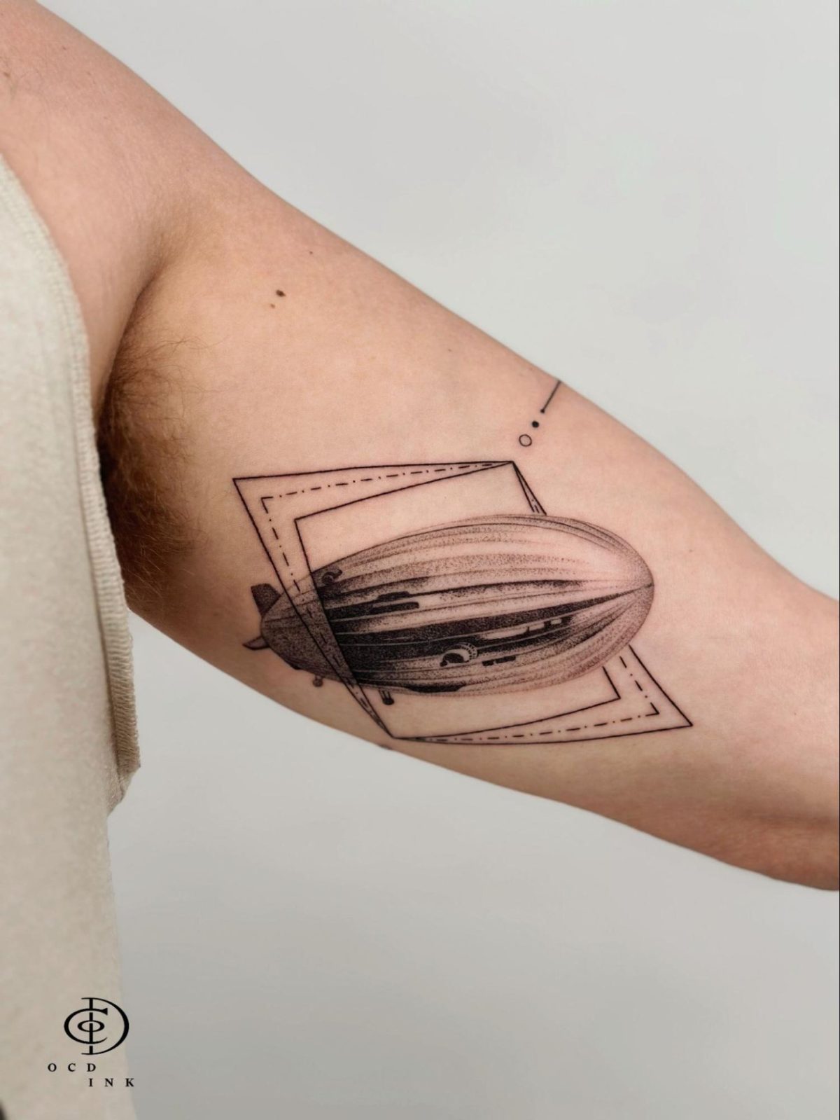 Micro realism dotwork tattoo of a vintage airship framed by geometric linework on the inner arm, featuring ultra-fine stipple shading and delicate black and grey details.