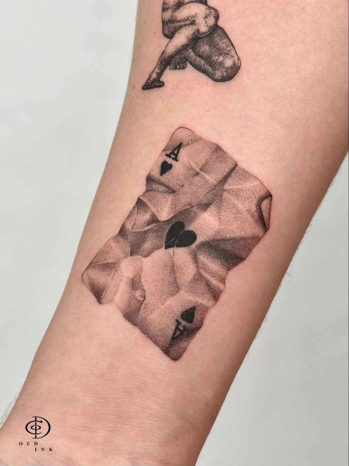 Micro realism dotwork tattoo of an Ace of Hearts playing card with a crumpled paper effect, created using fine stipple shading and black and grey realism.