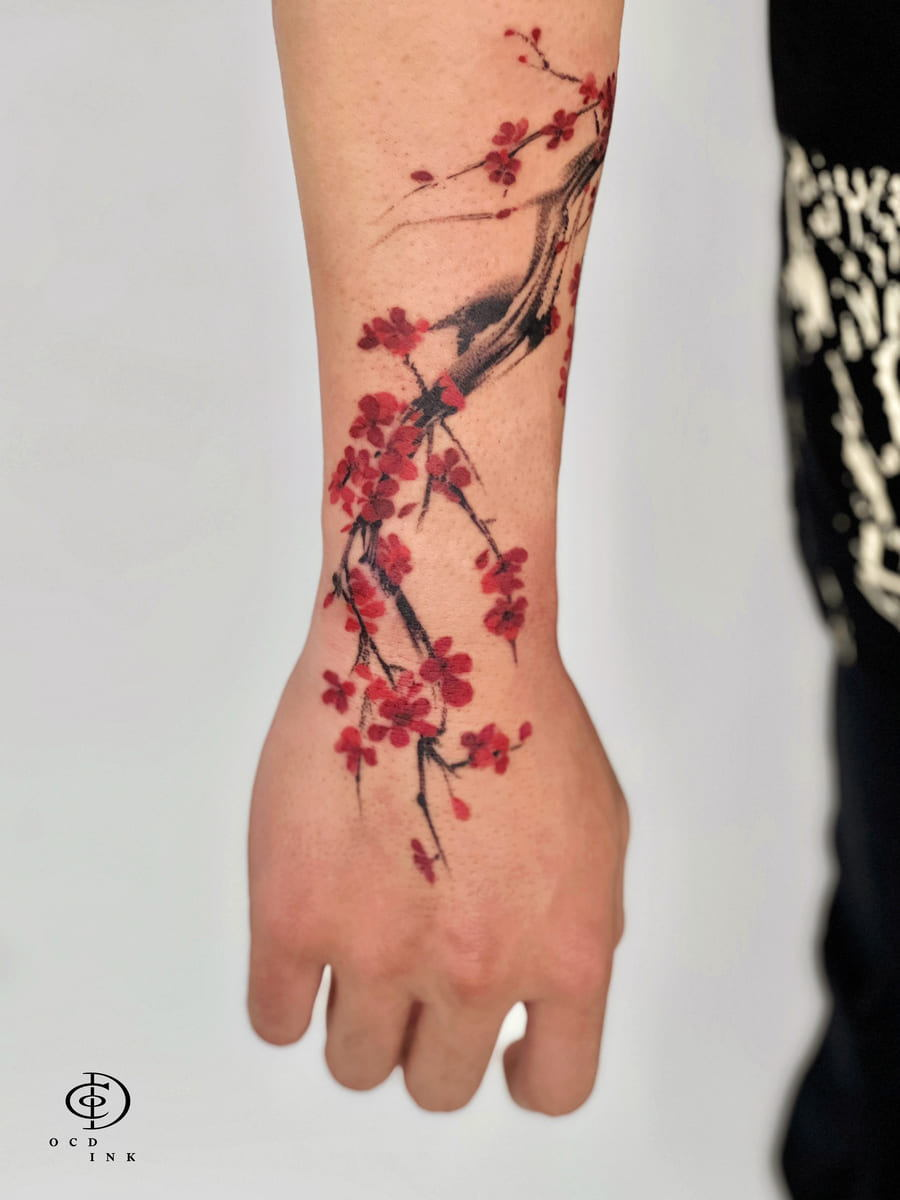 COLOR Cherry blossom tattoo featuring delicate red sakura flowers on black ink branches, combining watercolor-inspired color with expressive brushstroke linework.