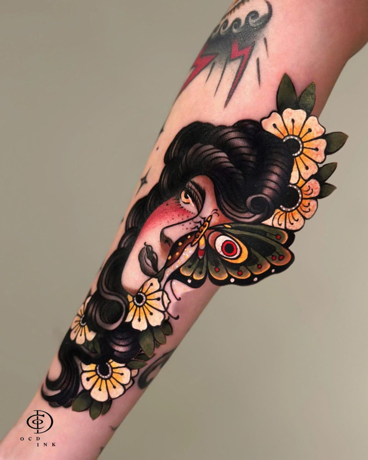 COLOR American traditional tattoo of a vintage woman's portrait with a butterfly across her face, surrounded by flowers and rendered with bold black outlines and muted colors.
