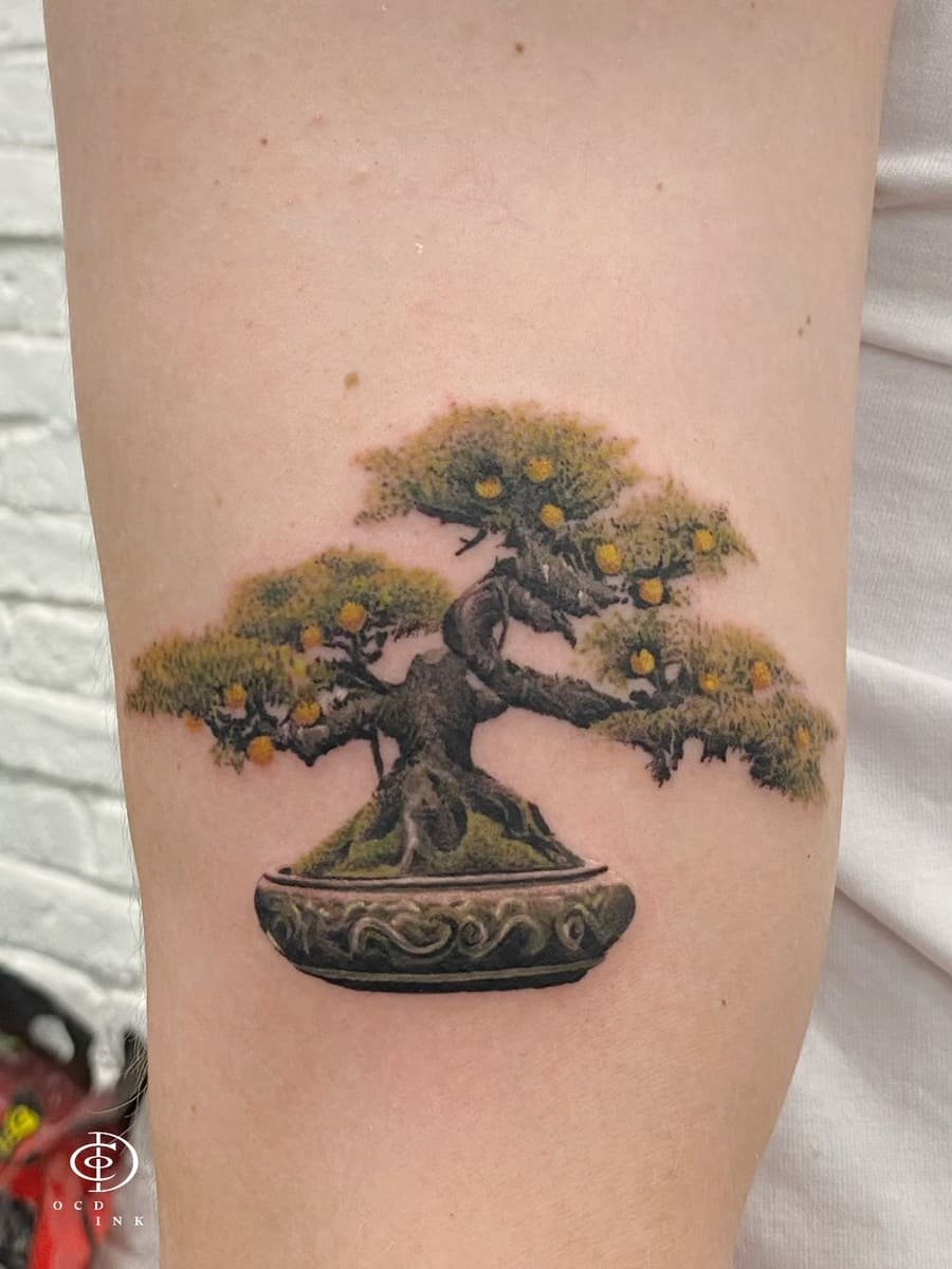 Color tattoo of a miniature bonsai tree in an ornate ceramic pot, featuring realistic bark texture, lush green foliage, and delicate yellow fruit on the upper arm.