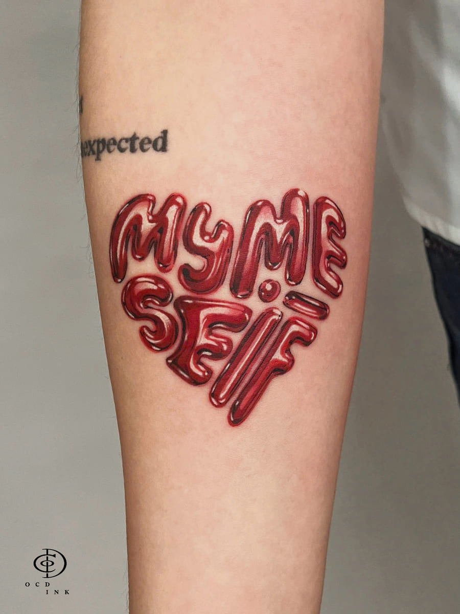 3D lettering tattoo spelling “MY ME SELF” in glossy red balloon-style typography, arranged in a heart shape with realistic highlights and shadows on the forearm.