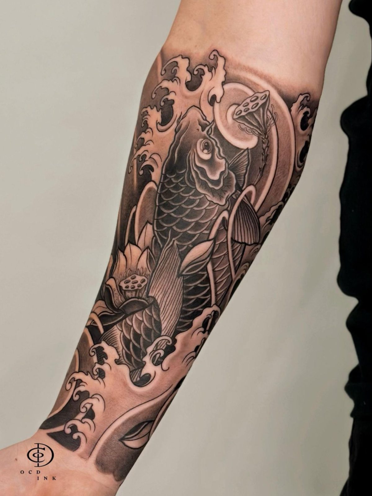 Black & Gray A black and gray Japanese-style koi fish sleeve tattoo featuring two detailed koi swimming through powerful waves with blooming lotus flowers and lotus seed pods