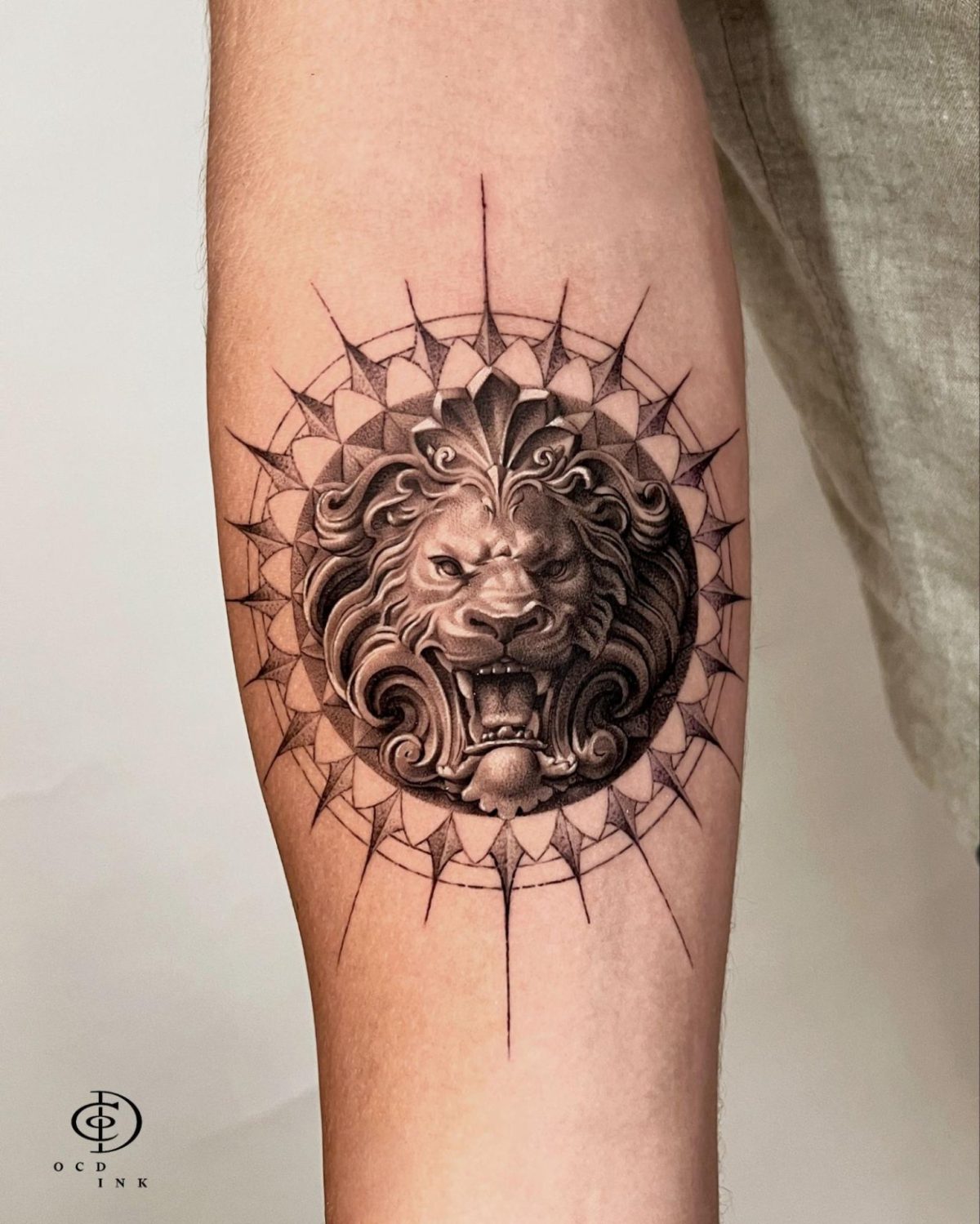 Black & Gray A black and gray realism tattoo of a roaring lion head framed by an intricate geometric mandala