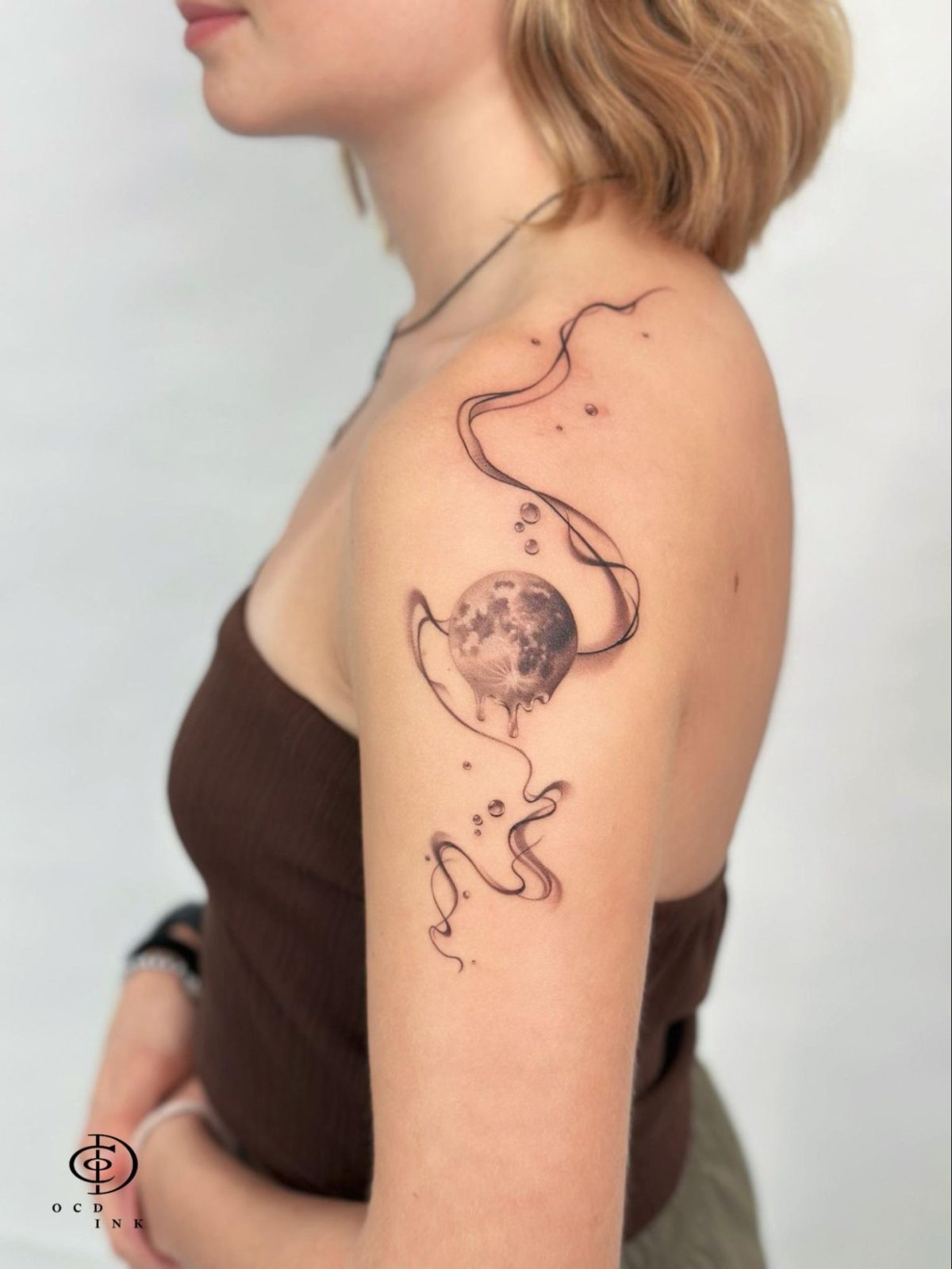 Black & Gray A minimalist black and gray tattoo of a melting moon with flowing abstract linework and delicate dot accents on the upper arm