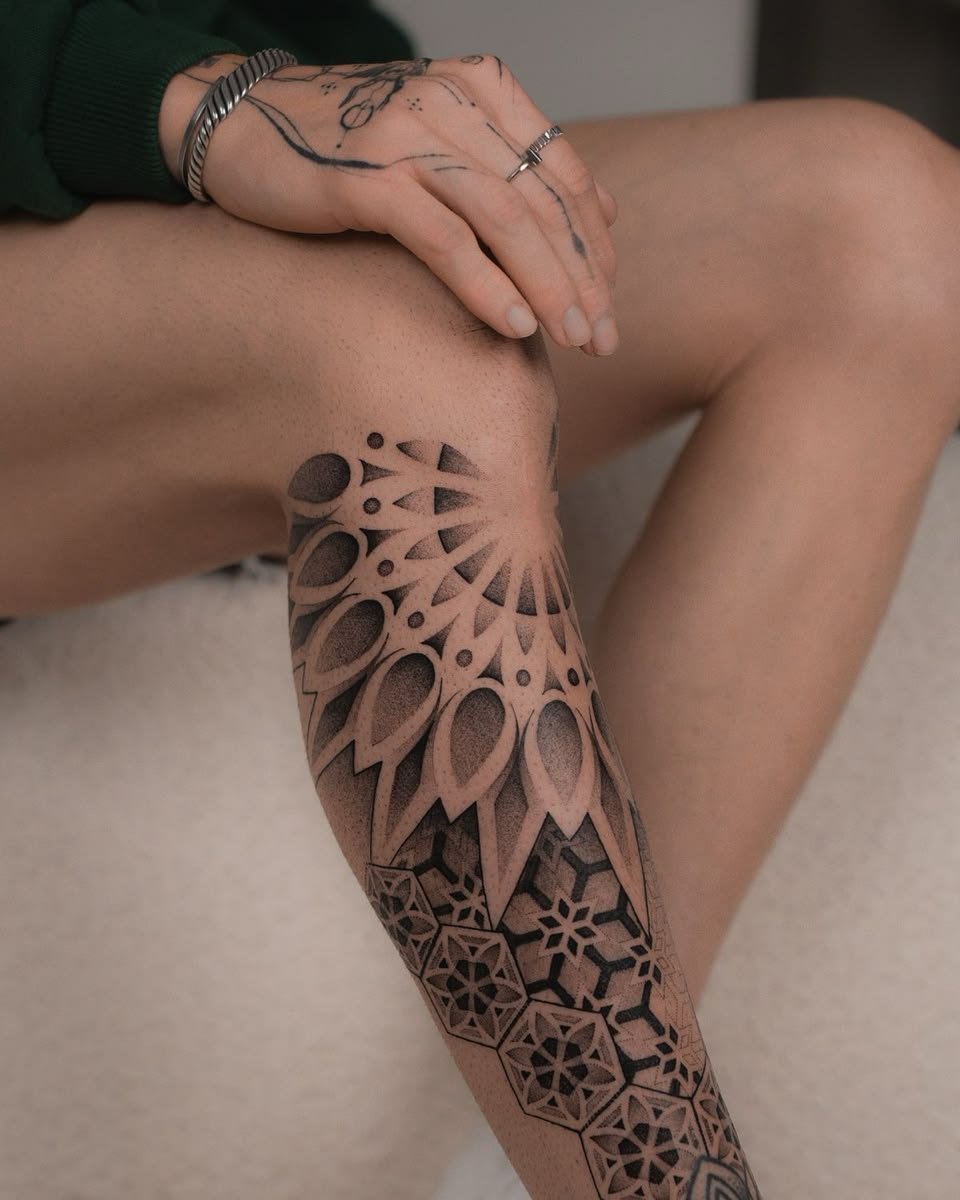 Black & Gray A black and gray geometric tattoo wrapping around the upper arm, featuring layered mandala-inspired patterns, dotwork shading, negative space, and intricate hexagonal motifs that create depth and symmetry.