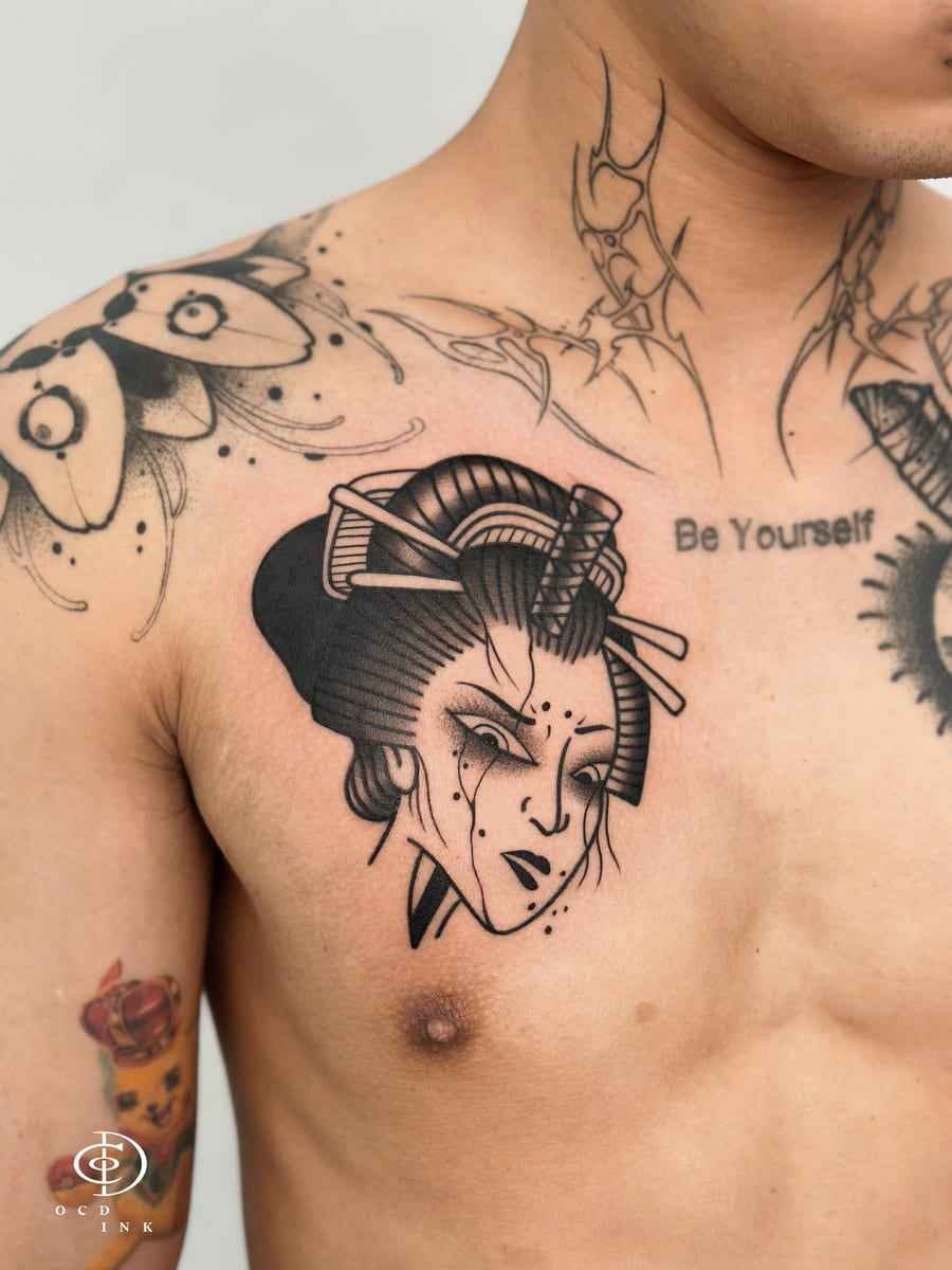 Blackwork traditional-inspired tattoo of a stylized geisha portrait on the chest, featuring dramatic facial details, ornamental hairpins, and graphic linework