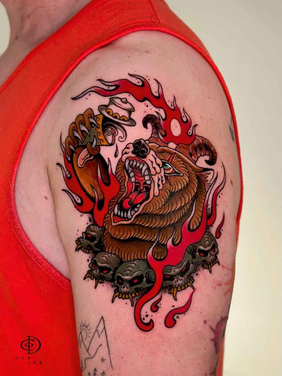Traditional-style tattoo of a roaring bear surrounded by vivid red flames and skull motifs on the upper arm.
