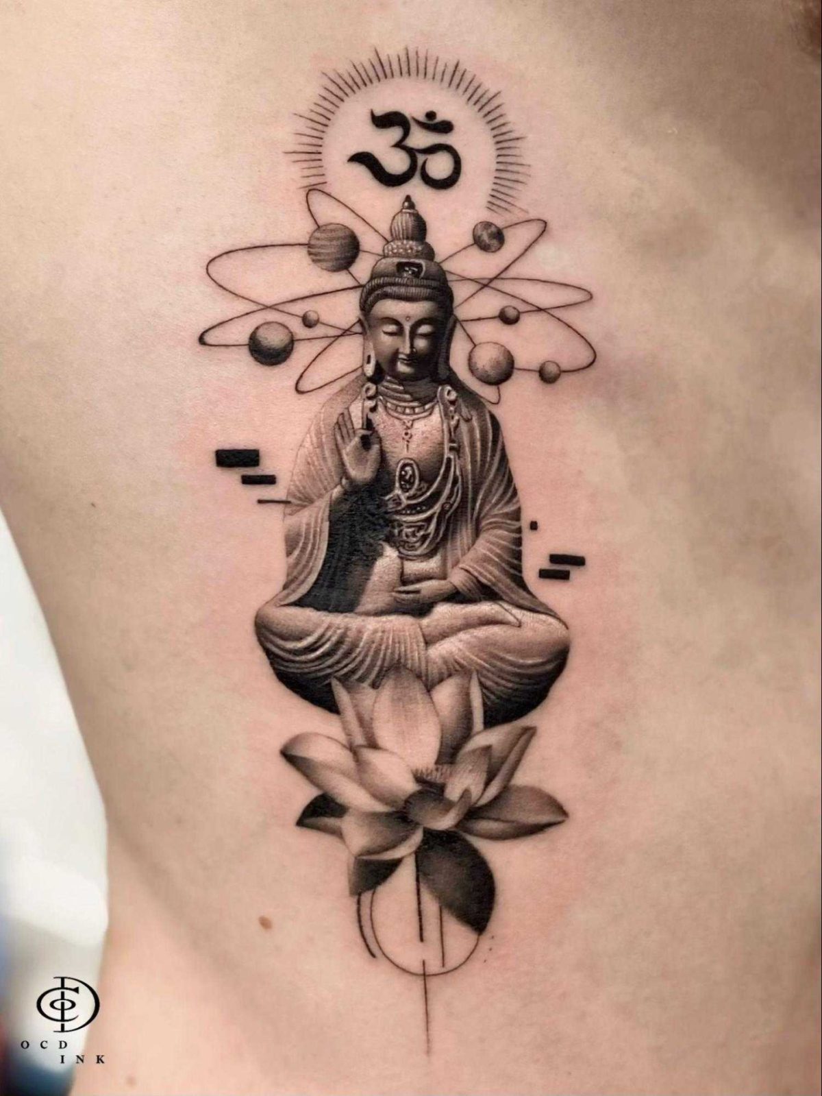 Black-and-grey graphic tattoo of a seated Buddha above a lotus, framed by planetary orbits and an Om symbol.