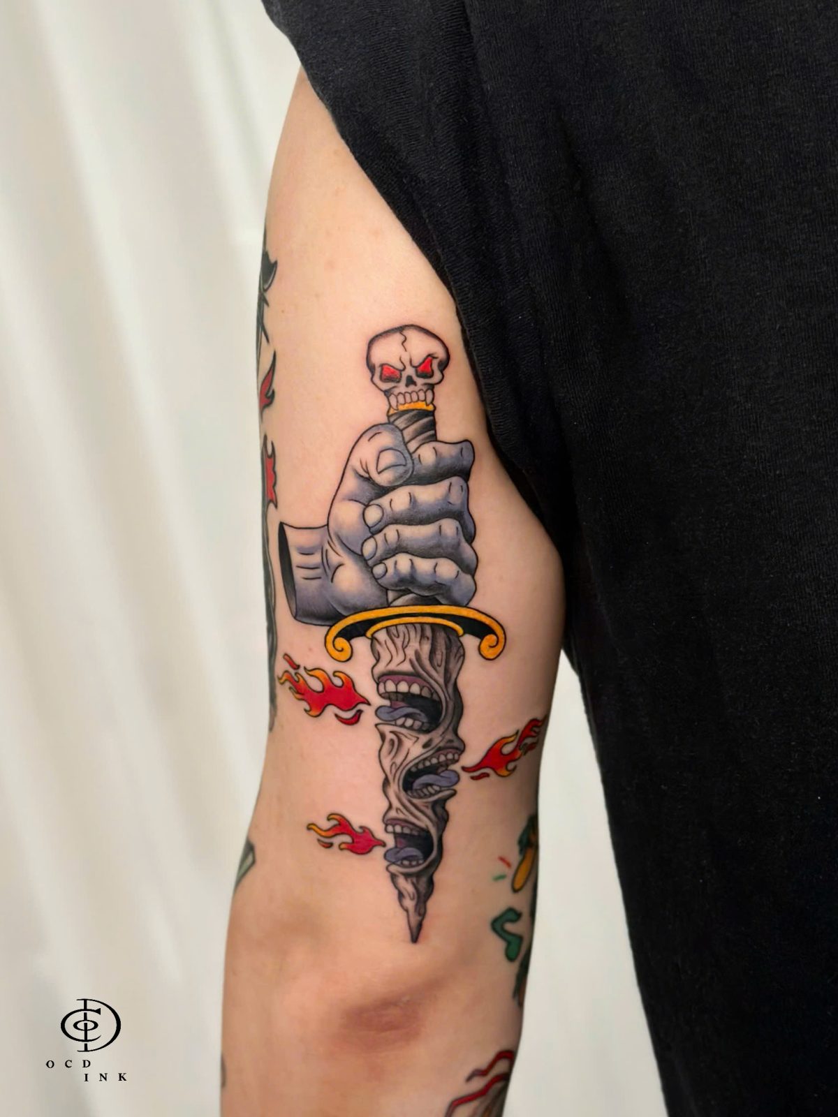 Traditional tattoo of a skeletal hand gripping a skull-shaped knife, combining bold black outlines, solid shading, and macabre illustrative details tattoo on the tricep by OCD Ink Studio in Hanoi