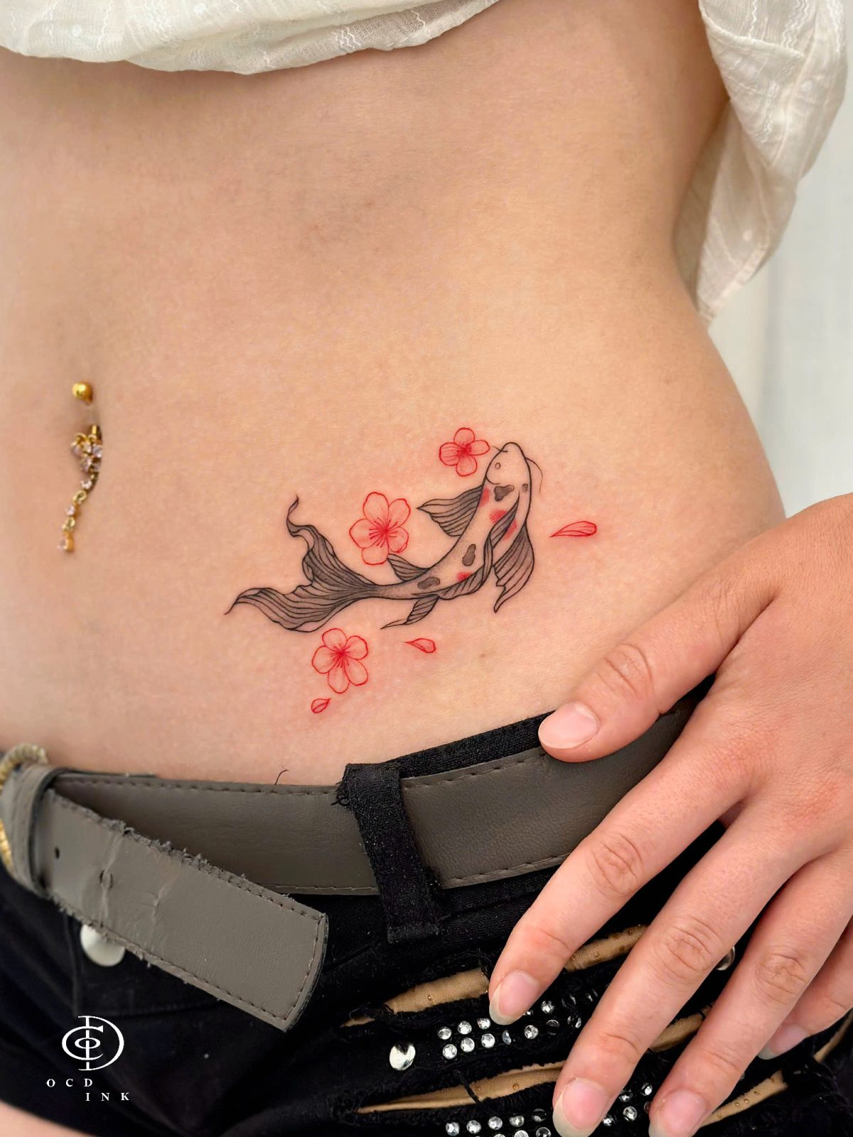 Fineline tattoo of a koi fish and blossoms, showcasing delicate scales, flowing curves, and elegant botanical details inspired by Japanese art tattoo on the hip by OCD Ink Studio in Hanoi